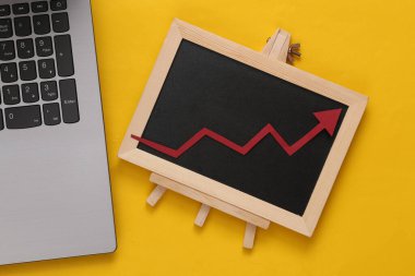 Laptop ve küçük tebeşir tahtası ve sarı arka planda bir büyüme oku. İş konsepti
