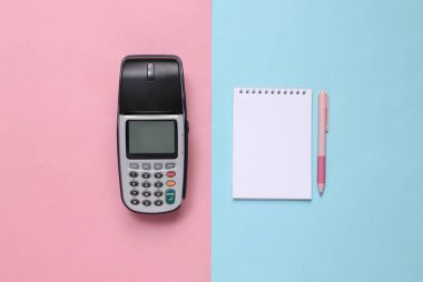 Ödeme terminali ve mavi-pembe renkli arka planda bir defter. Üst görünüm.