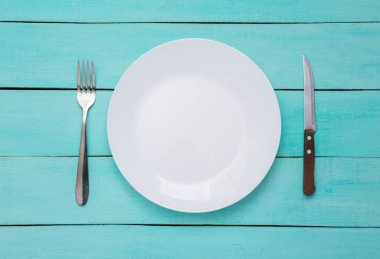 Mavi ahşap arka planda çatal ve bıçaklı bir tabak. Üst görünüm