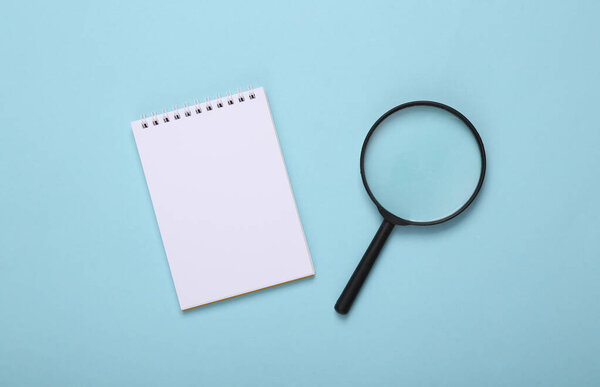 Notepad and magnifier on a blue background. Top view