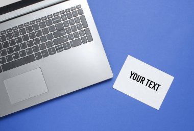 Mavi arkaplanda kopyalama alanı için modern laptop ve beyaz kağıt. Üst görünüm