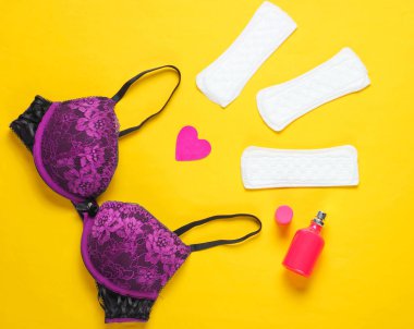 Kadınların kritik günleri, adet günleri. Minimalist kadın hijyen konsepti. Güzel seksi sutyen, külotlu çorap, parfüm şişesi, sarı arka planda kalp.