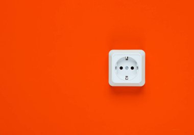 Turuncu arka planda beyaz plastik priz. Kopya alanı olan duvar. Minimalizm