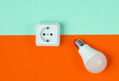 Beyaz plastik priz ve mavi turuncu arka planda LED ampul. Minimalizm. Üst görünüm