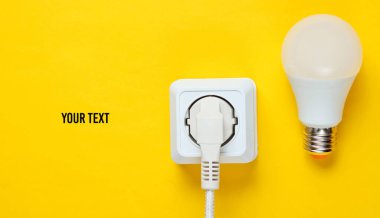 Elektrik prizine bağlı beyaz kablo ve fotokopi alanı olan sarı zemin üzerindeki LED ampulü. Üst görünüm