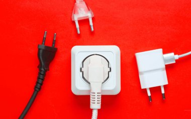 Elektrik bağımlılığı kavramı. Kırmızı arkaplanda elektrik prizlerinin yanında bir sürü elektrik prizi var