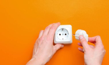 Kadın eli, turuncu arka plandaki elektrik prizine takılır. Minimalizm. Üst görünüm