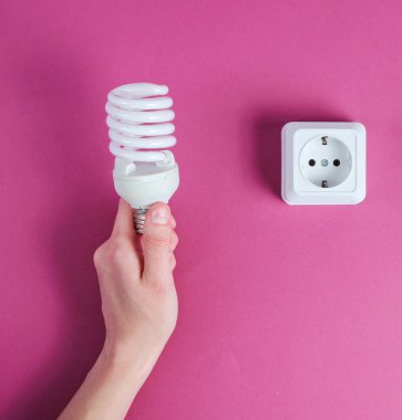 Mor arka planda el ele tutuşan spiral ampul. Minimalizm