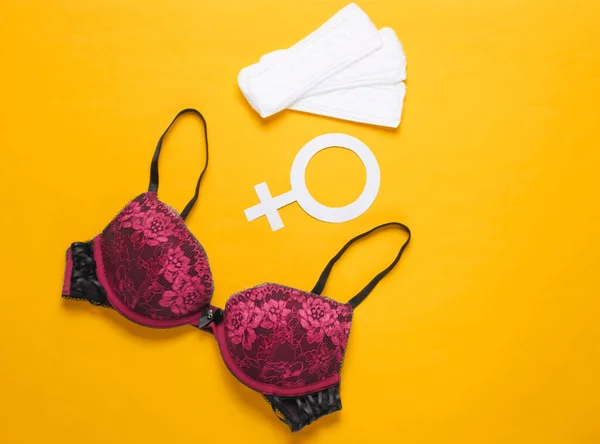 Women\'s critical days, menstruation. Minimalistic feminine hygiene concept. Beautiful sexy bra, panty liners, gender symbol on yellow