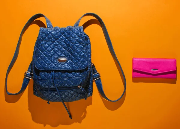 Leather backpack with straps and pink purse on orange background. Top view, minimalism fashion