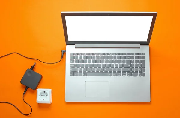 Female hand plugs a laptop charger into an electrical outlet on orange background