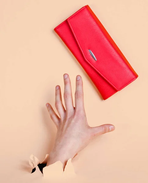 Female hand takes red purse through torn yellow pastel paper. Minimalistic creative fashion concept