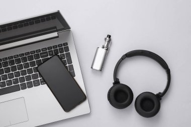 Dizüstü bilgisayarın düz kompozisyonu, noyshniks, akıllı telefon ve gri arka planda bir buhar cihazı. Modern aletler. Üst görünüm