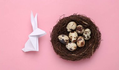 Paskalya kompozisyonu. Origami Paskalya tavşanı ve bıldırcın yumurtaları pembe pastel arka planda. Üst görünüm
