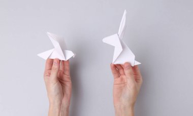 Eller el ele tutuşmuş origami tavşanı ve gri arka planda güvercin.
