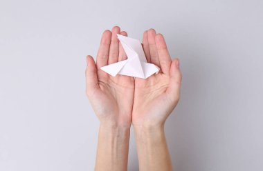 Gri arka planda el ele tutuşan origami güvercini. Barış sembolü, dikkat