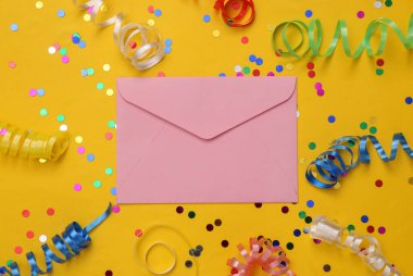 Renkli şeritli zarf ve sarı arka planda konfeti. Tatil, doğum günü geçmişi