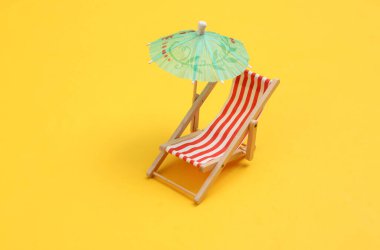 Sarı arka planda şemsiyesi olan mini plaj koltuğu. Sahil tatili, yaz tatili, güneşlenme konsepti.