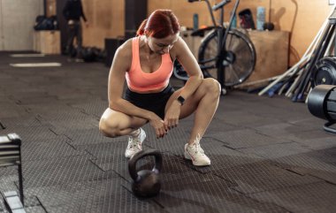 Spor salonunda kettlebell ile yapılan yoğun antrenmandan sonra yorgun ve zinde bir kadın dinleniyor.
