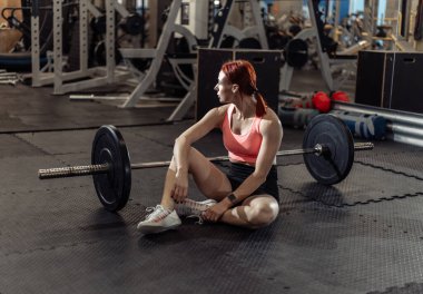 Spor salonunda halterle yapılan yoğun egzersizden sonra dinlenen atletik kadın.