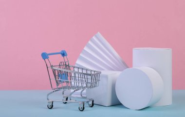 Alışveriş arabası ve geometrik şekiller mavi pembe pastel arka planda. Satış, ürün sunumu. Soyut arka plan, konsept sanat, minimalizm. Geometrik bileşim
