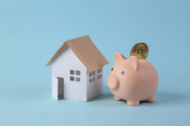 Mavi arka planda bitcoin ve model evi olan domuz kumbarası. Tasarruf kavramı
