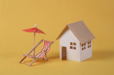 Şemsiyeli iskemle ve sarı arka planda ev modeli. Ev istirahatı 