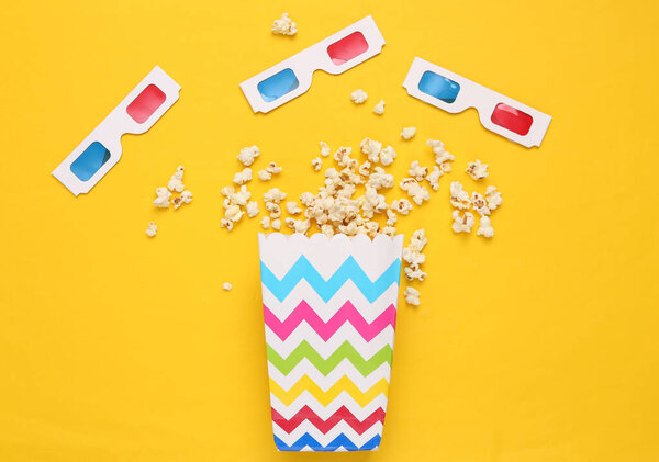 Popcorn bucket and 3D glasses on yellow background. Top view. Flat lay