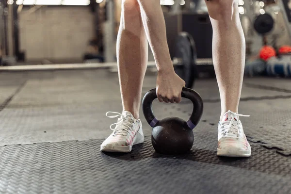 Spor salonunda bir kadının eli ağır bir kettlebell tutuyor.