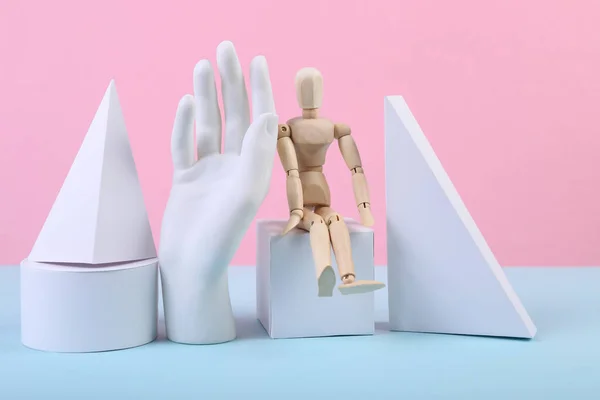 Geometric figures, wooden puppet and hand on a blue-pink pastel background. Composition of different geometric objects. Concept art. Abstract background, minimalism