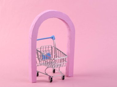 Pembe arka planda kemer ve alışveriş arabası olan minimalist bir sahne. Minimalizm, yaratıcı alışveriş kavramı