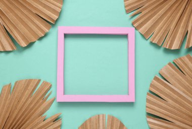 Mavi arka planda pembe çerçeve ve kuru palmiye yaprakları. Metin için boşluk