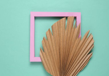 Mavi arkaplanda pembe çerçeve ve kuru palmiye yaprağı.