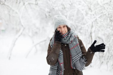 Sıcak elbiseli bir kadın açık havada karlı kış havasında telefonda konuşuyor. 