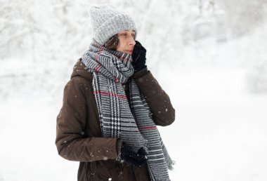 Sıcak elbiseli bir kadın açık havada karlı kış havasında telefonda konuşuyor. 