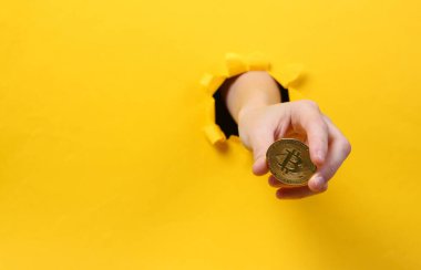 Kadın eli, bitcoin 'i yırtık sarı kağıttan tutuyor. Sanat kavramı
