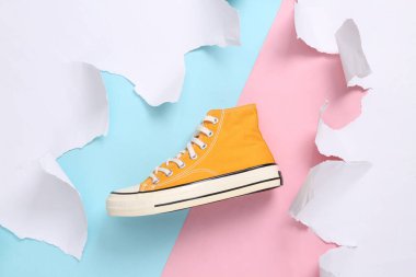 Retro yellow Sneaker with white torn paper sheets on pink blue background. Minimalistic creative background.