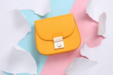 Yellow leather bag on blue-pink background with torn paper. Concept art. Pastel color trend. Top view