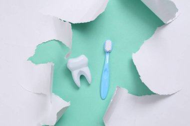 Toy tooth and toothbrush on blue background with white torn paper. Minimalism. Top view