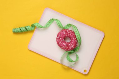 Slimming concept. Delicious high-calorie donut and measuring ruler on a yellow background. Losing weight.