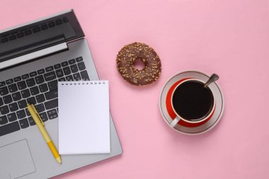 Flat lay composition of laptop, notebook, coffee cup and donuts on pink background. Top view