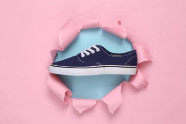 Sneaker through a torn hole on a blue-pink pastel background. Concept art. Pastel color trend. Minimalism