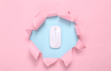 Pc mouse through torn hole on blue-pink pastel background. Business concept. Pastel color trend. Minimalism