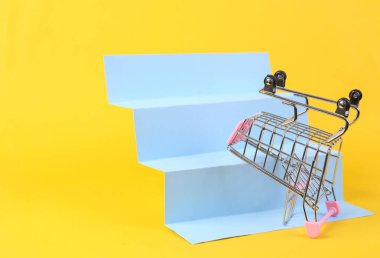 Shopping trolley on stairs, yellow background. Concept art, minimalism