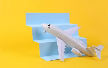 Toy air plane on stairs podium, yellow background. Travel Concept, minimalism