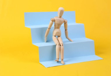 Wooden puppet on stairs podium, yellow background. Concept art, minimalism