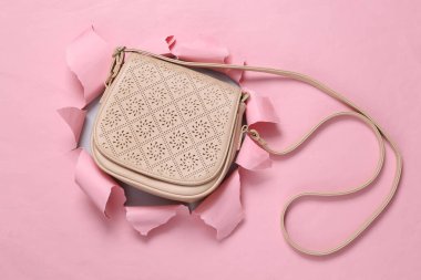 Fashion concept. Leather yellow bag on pink paper background with torn hole