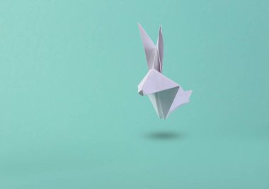 Origami tavşanı mavi arka planda havada süzülüyor. Üç boyutlu fotoğraf. Yaratıcı sanat. Minimalizm paskalya konsepti 