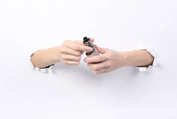 Female hands holding vaping device through torn hole white paper. Concept art