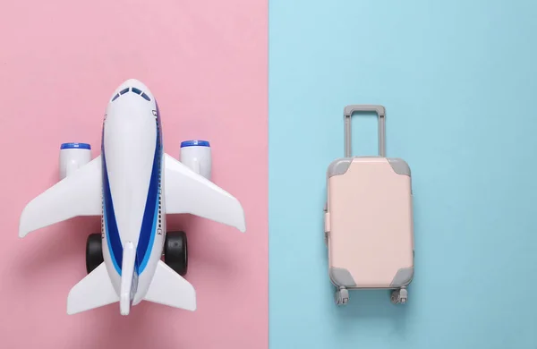 Travel flat lay. Toy passenger plane and luggage on a blue-pink pastel background. Top view